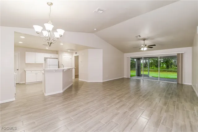 a view of an empty room with wooden floor and a kitchen