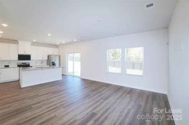 a kitchen with stainless steel appliances granite countertop a stove top oven a sink and white cabinets with wooden floor next to windows