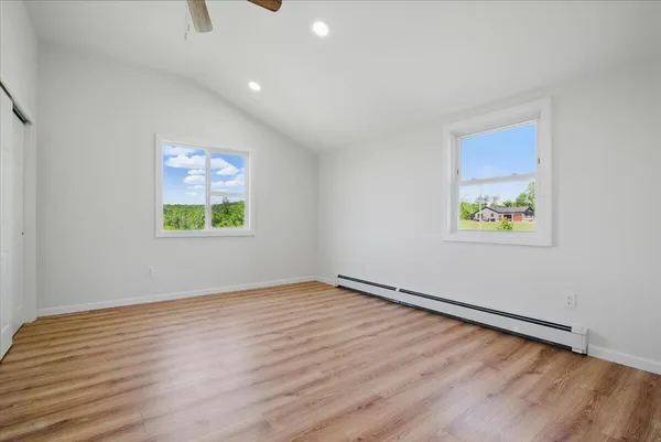 an empty room with wooden floor ceiling fan and windows