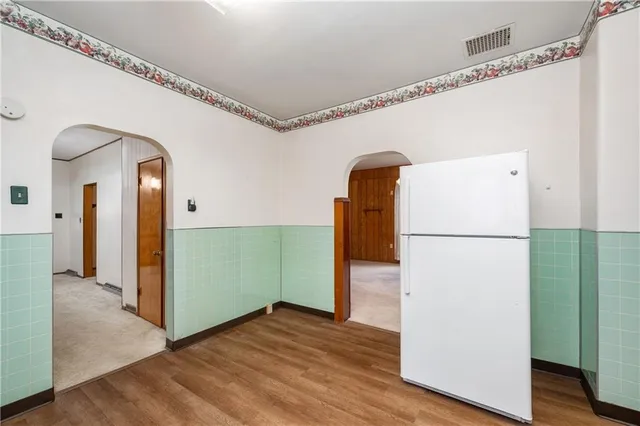 a view of a refrigerator in kitchen and an empty room with wooden floor