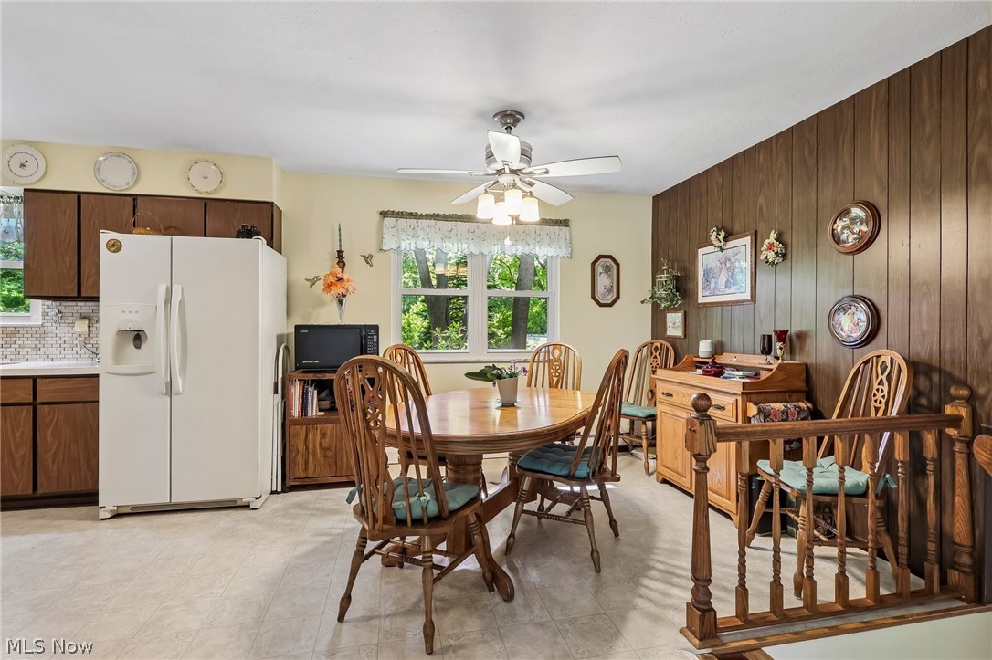 2428 Antioch Road Perry, OH 44081 - Photo 19 of 46 Open-concept kitchen and dining area featuring warm wood-finish cabinetry, a patterned tile backsplash, a ceiling fan with integrated lighting, and a wood-paneled accent wall
