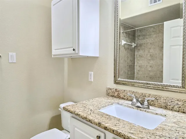 a bathroom with a granite countertop sink a toilet and a mirror