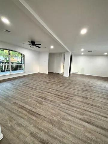 an empty room with wooden floor and kitchen view