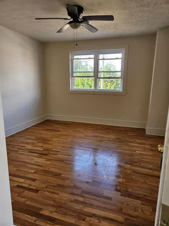 an empty room with wooden floor chandelier fan and windows