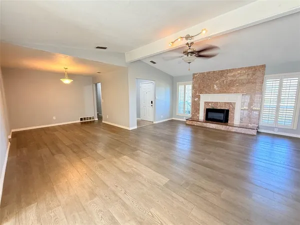 an empty room with wooden floor fireplace and windows