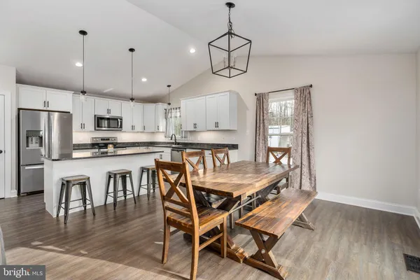 a dining room with stainless steel appliances kitchen island granite countertop a table chairs and a refrigerator