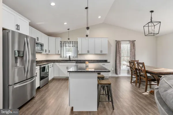 a kitchen with stainless steel appliances a refrigerator a stove a sink dishwasher a dining table and chairs with wooden floor