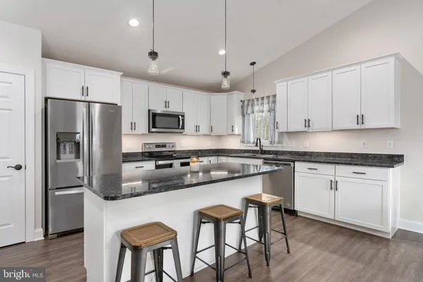 a kitchen with stainless steel appliances granite countertop a refrigerator a stove a sink dishwasher a stove and white cabinets with wooden floor