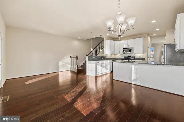 a kitchen with stainless steel appliances granite countertop a stove top oven a sink dishwasher and a dining table with wooden floor