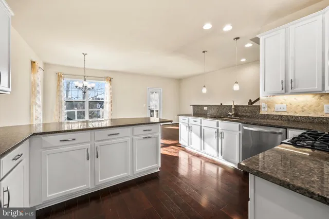 a large kitchen with granite countertop a stove a sink a refrigerator and white cabinets with wooden floor