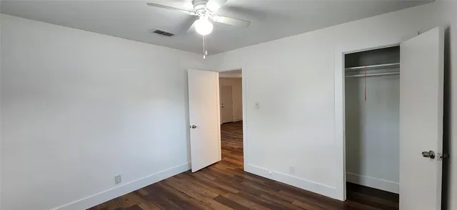 an empty room with wooden floor closet and windows