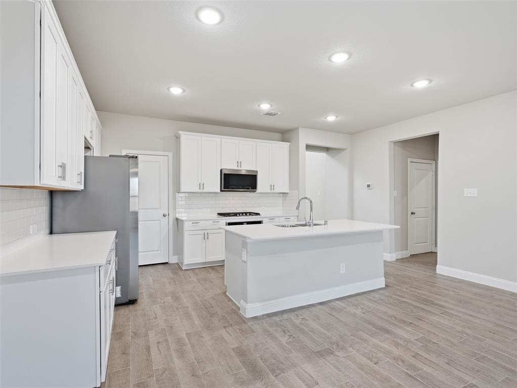 1128 Red Hawk Lane Forney, TX 75126 - Photo 9 of 37 Kitchen featuring white cabinetry, light-toned countertops, a center island with sink, stainless steel appliances, and wood-finish flooring