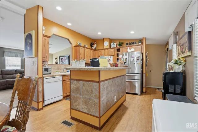 a kitchen with stainless steel appliances kitchen island granite countertop dining table chairs and a refrigerator