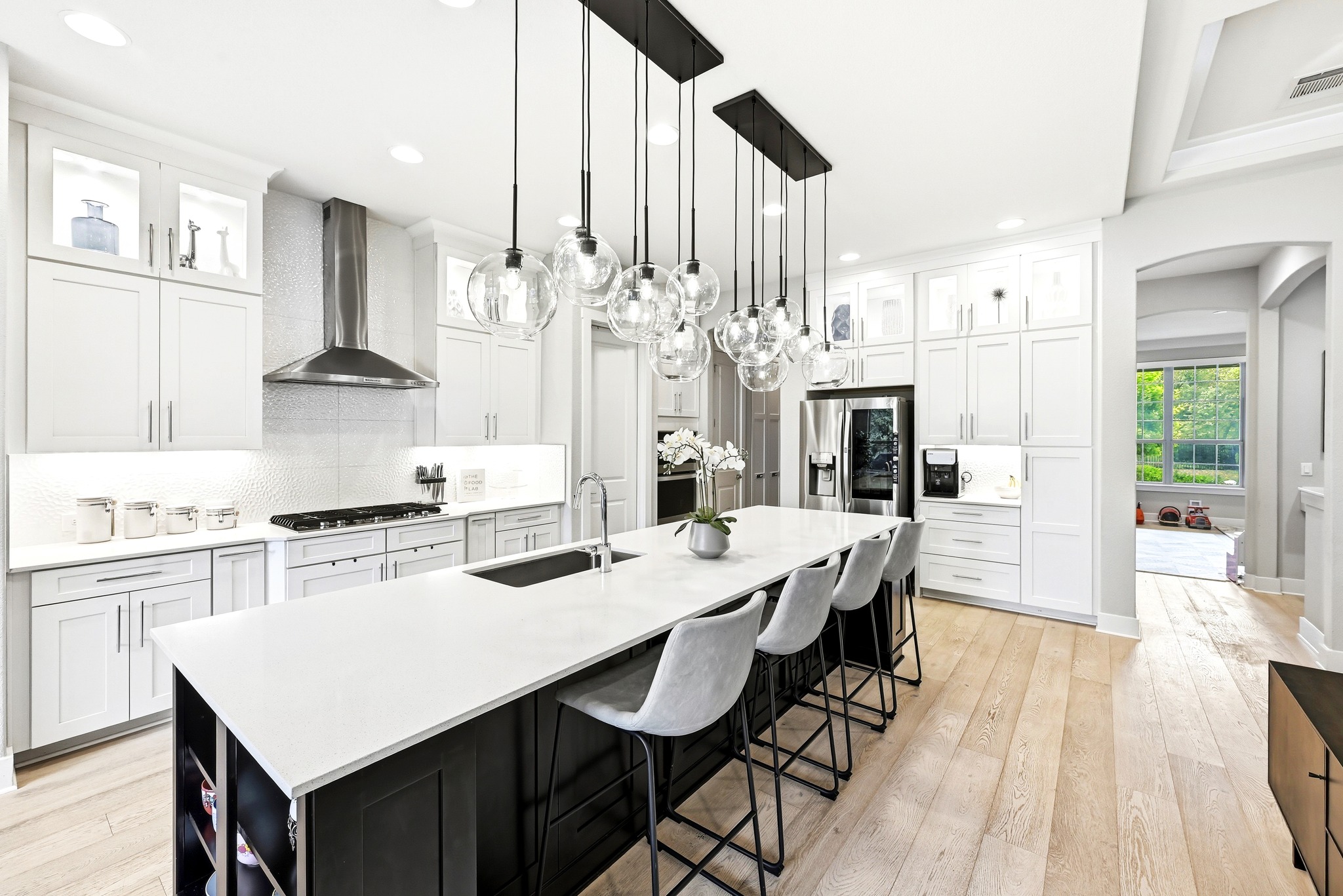 9008 Harper Rae Drive Austin, TX 78717 - Photo 12 of 39 Spacious kitchen featuring an oversized island with countertop seating, light wood-finish flooring, white perimeter cabinetry, stainless steel appliances, and statement pendant lighting