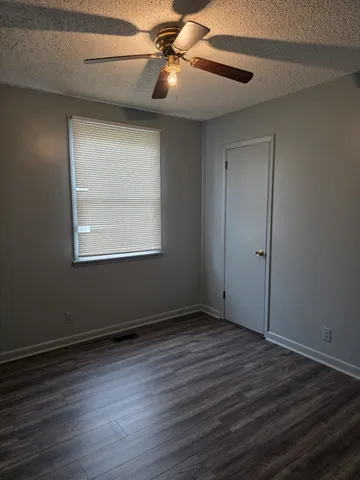 an empty room with wooden floor chandelier fan and windows