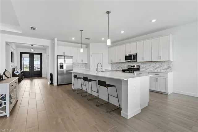 a kitchen with stainless steel appliances kitchen island granite countertop a stove a sink a refrigerator and white cabinets with wooden floor