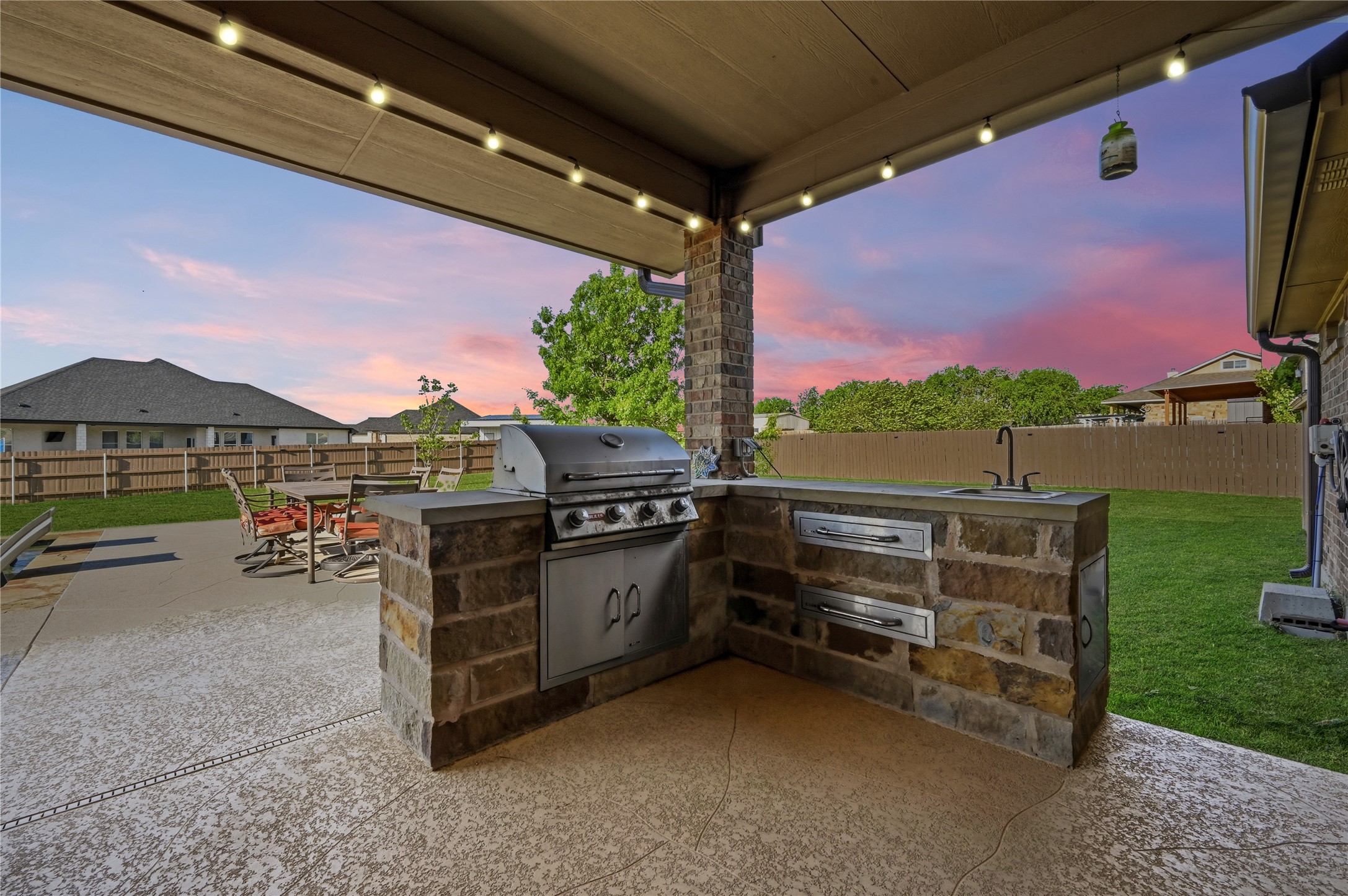 4467 West Amity Road Salado, TX 76571 - Photo 30 of 40 Outdoor kitchen featuring a built-in grill, sink, and stone facade, all under a covered patio with string lights