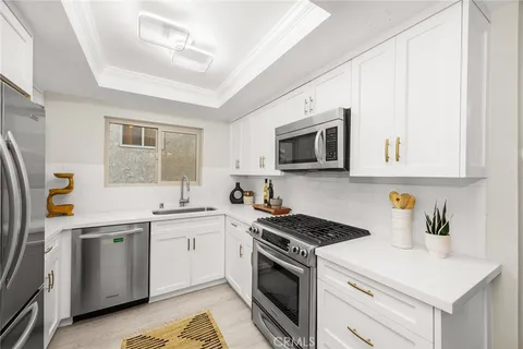a kitchen with stainless steel appliances a white stove top oven a sink dishwasher and white cabinets with wooden floor