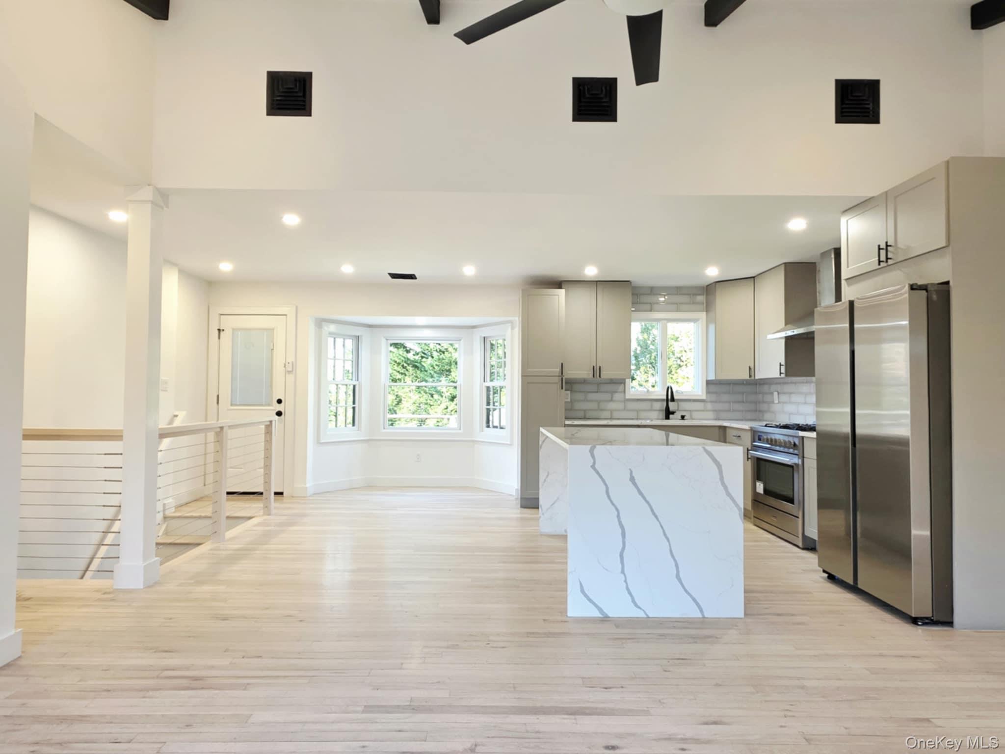 185 Wakeman Road Hampton Bays, NY 11946 - Photo 3 of 19 Kitchen with appliances with stainless steel finishes, light stone counters, wall chimney range hood, light wood-style floors, and gray cabinets
