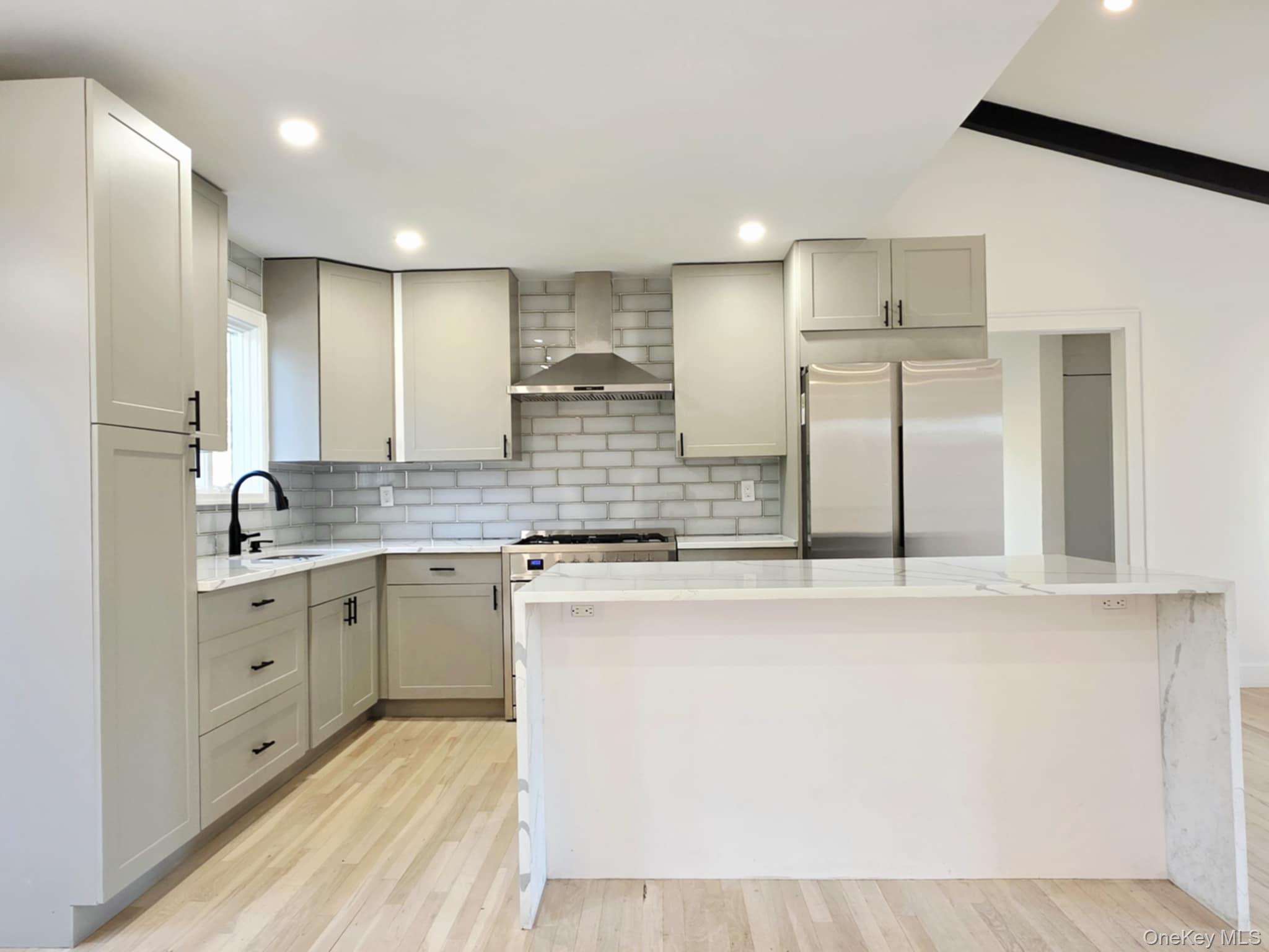 185 Wakeman Road Hampton Bays, NY 11946 - Photo 4 of 19 Kitchen with light stone countertops, appliances with stainless steel finishes, wall chimney exhaust hood, a kitchen island, and light wood-style floors