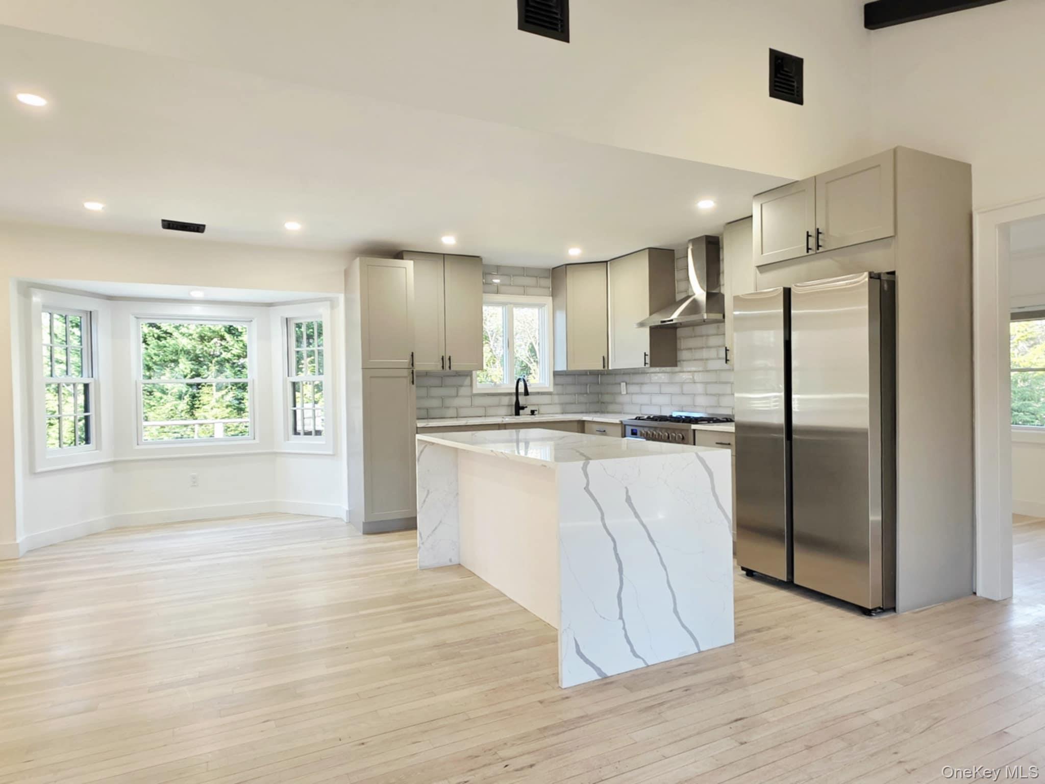 185 Wakeman Road Hampton Bays, NY 11946 - Photo 8 of 14 Kitchen featuring a kitchen island, stainless steel appliances, gray cabinetry, light stone counters, and wall chimney exhaust hood