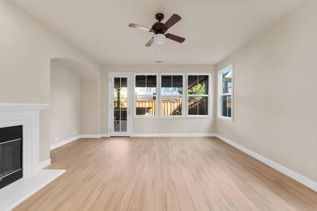 an empty room with wooden floor a ceiling fan and windows