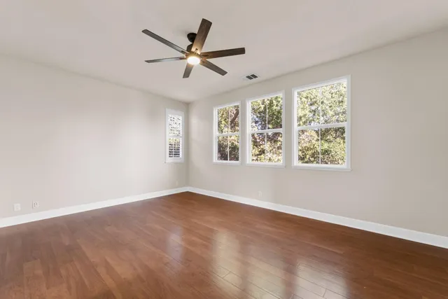 an empty room with wooden floor fan and windows