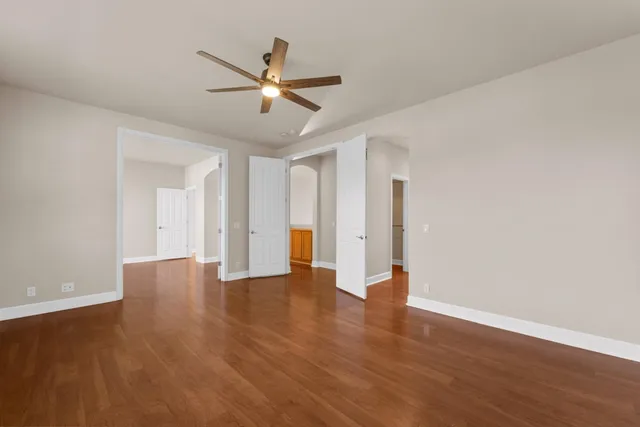 a view of an empty room with wooden floor and a ceiling fan