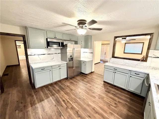 a living room with stainless steel appliances furniture a rug and a kitchen view