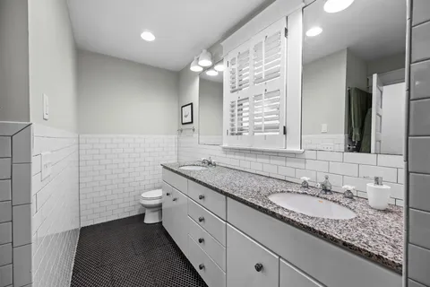 a bathroom with a granite countertop double vanity sink a mirror and a toilet
