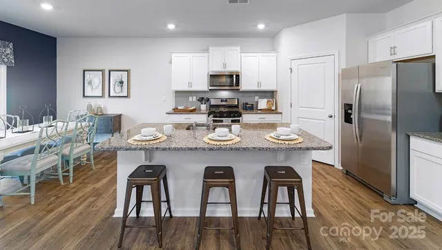 a kitchen with stainless steel appliances granite countertop a dining table chairs refrigerator and microwave