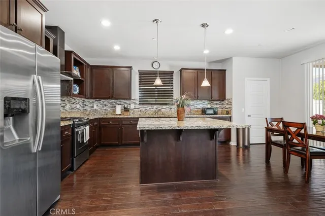 a kitchen with stainless steel appliances granite countertop a stove a sink dishwasher a refrigerator and a dining table with wooden floor