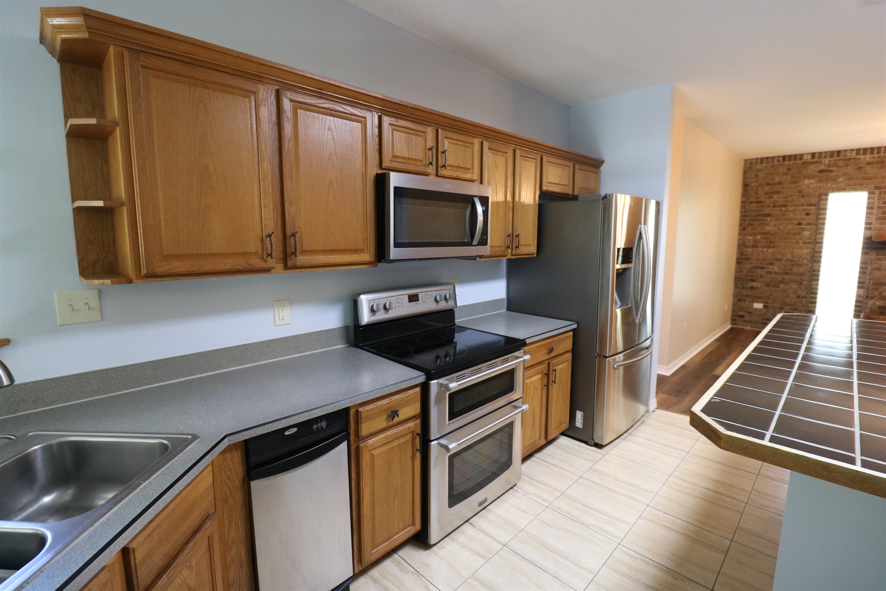 5861 Datil Pepper Road St. Augustine, FL 32086 - Photo 8 of 27 Kitchen featuring open shelves, brown cabinets, dark countertops, appliances with stainless steel finishes, and brick wall