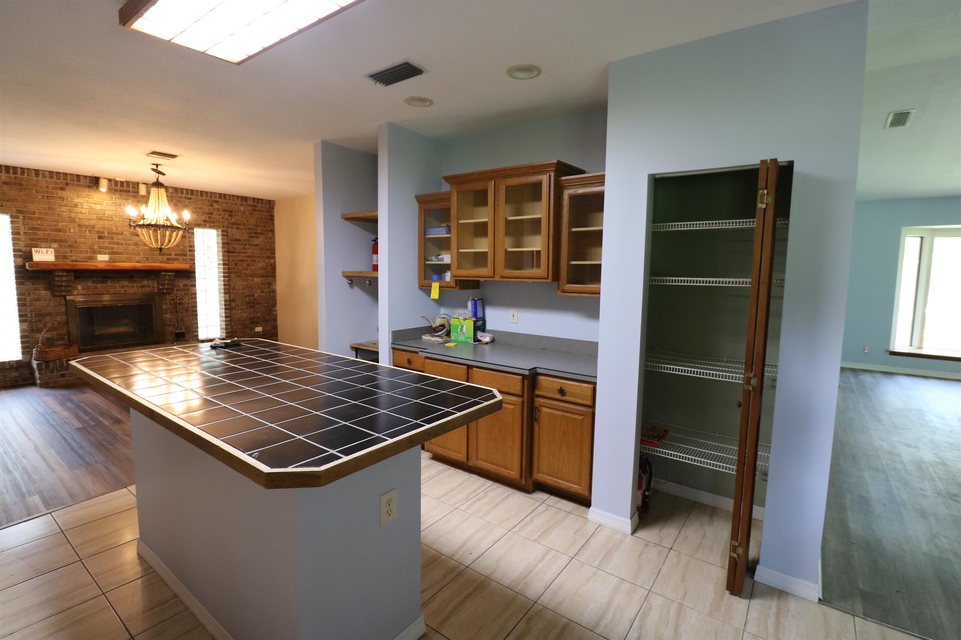 5861 Datil Pepper Road St. Augustine, FL 32086 - Photo 10 of 27 Kitchen with brown cabinets, brick wall, open shelves, tile countertops, and a brick fireplace