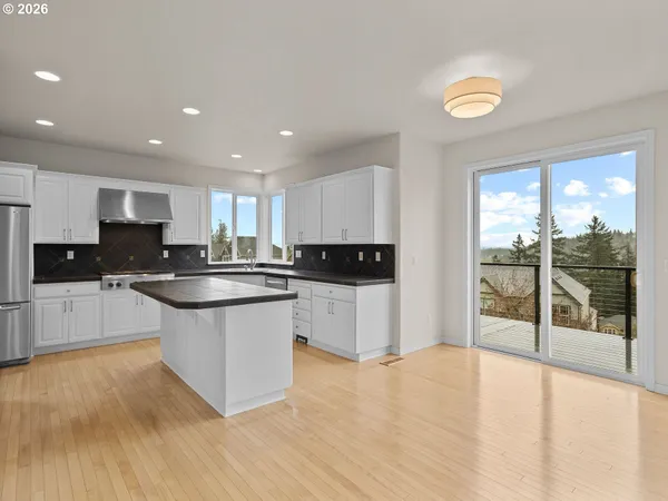 a large kitchen with kitchen island granite countertop a stove a sink a refrigerator and white cabinets with wooden floor