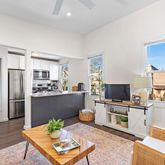 a living room with stainless steel appliances furniture a rug and a kitchen view