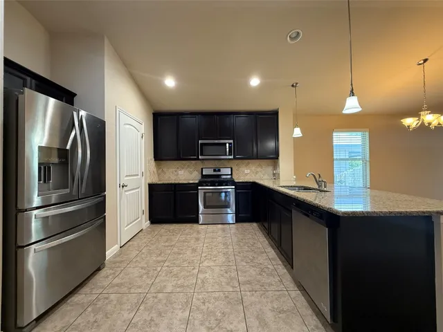 a large kitchen with a large kitchen island a sink dishwasher a refrigerator and a oven with wooden floor