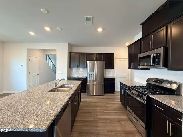 a kitchen with stainless steel appliances granite countertop a stove top oven a sink dishwasher a refrigerator and cabinets with wooden floor