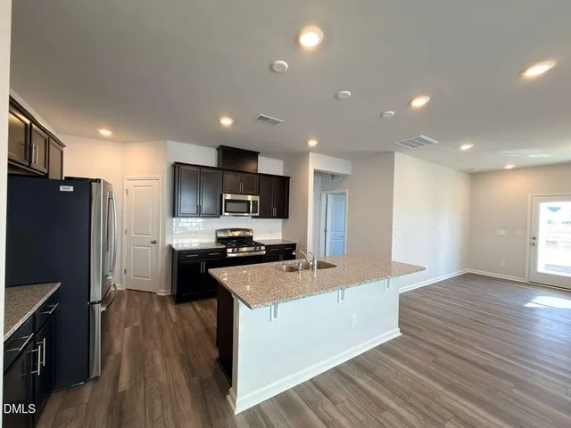 a large kitchen with stainless steel appliances a refrigerator a stove top oven a sink dishwasher and wooden floor