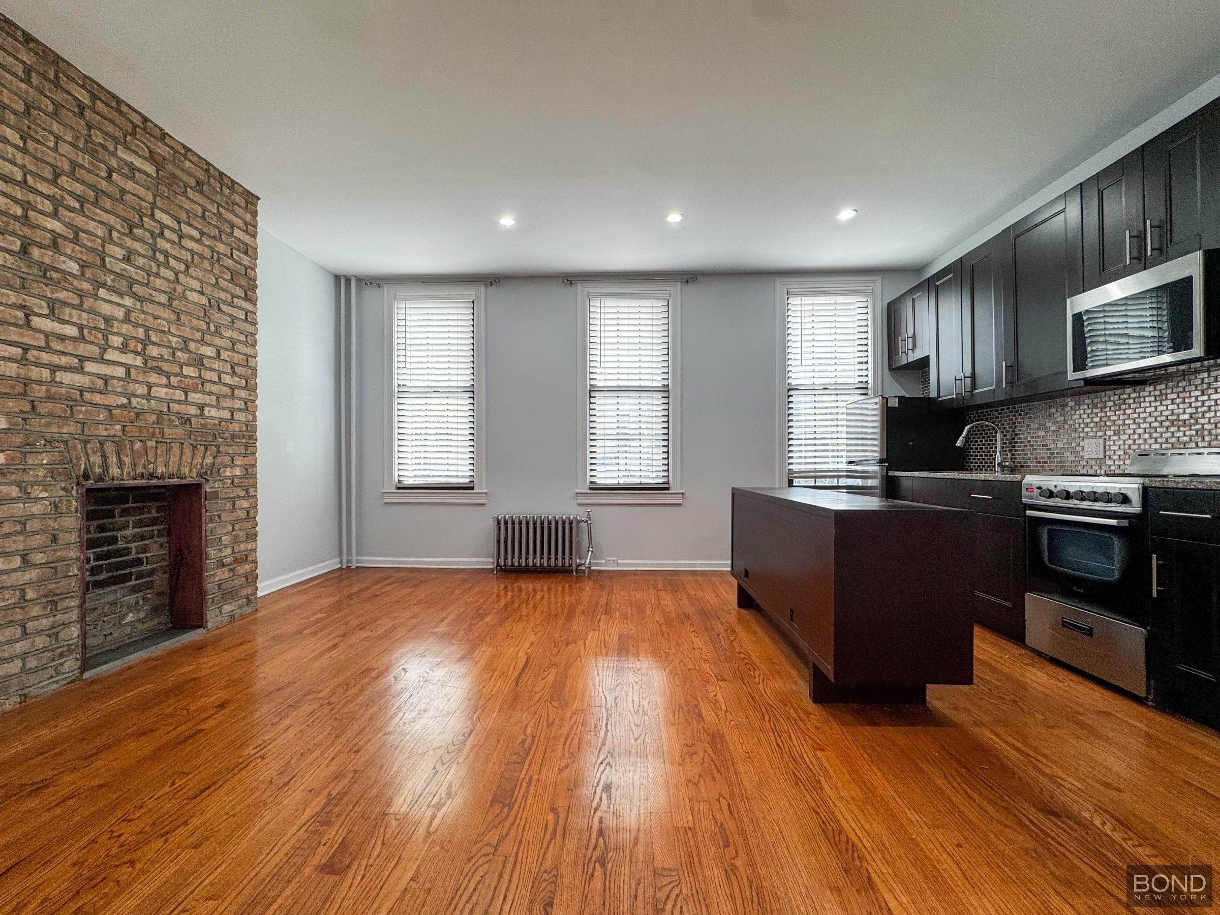 19-21 Gates Avenue, Unit 1F Queens, NY 11385 - Photo 1 of 10 a large kitchen with stainless steel appliances granite countertop a stove a sink dishwasher a microwave oven with cabinets and wooden floor