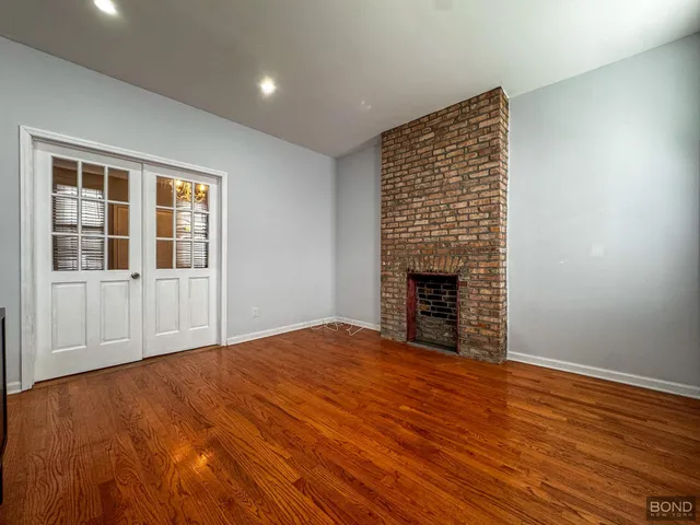 a view of an empty room with wooden floor fireplace and a window