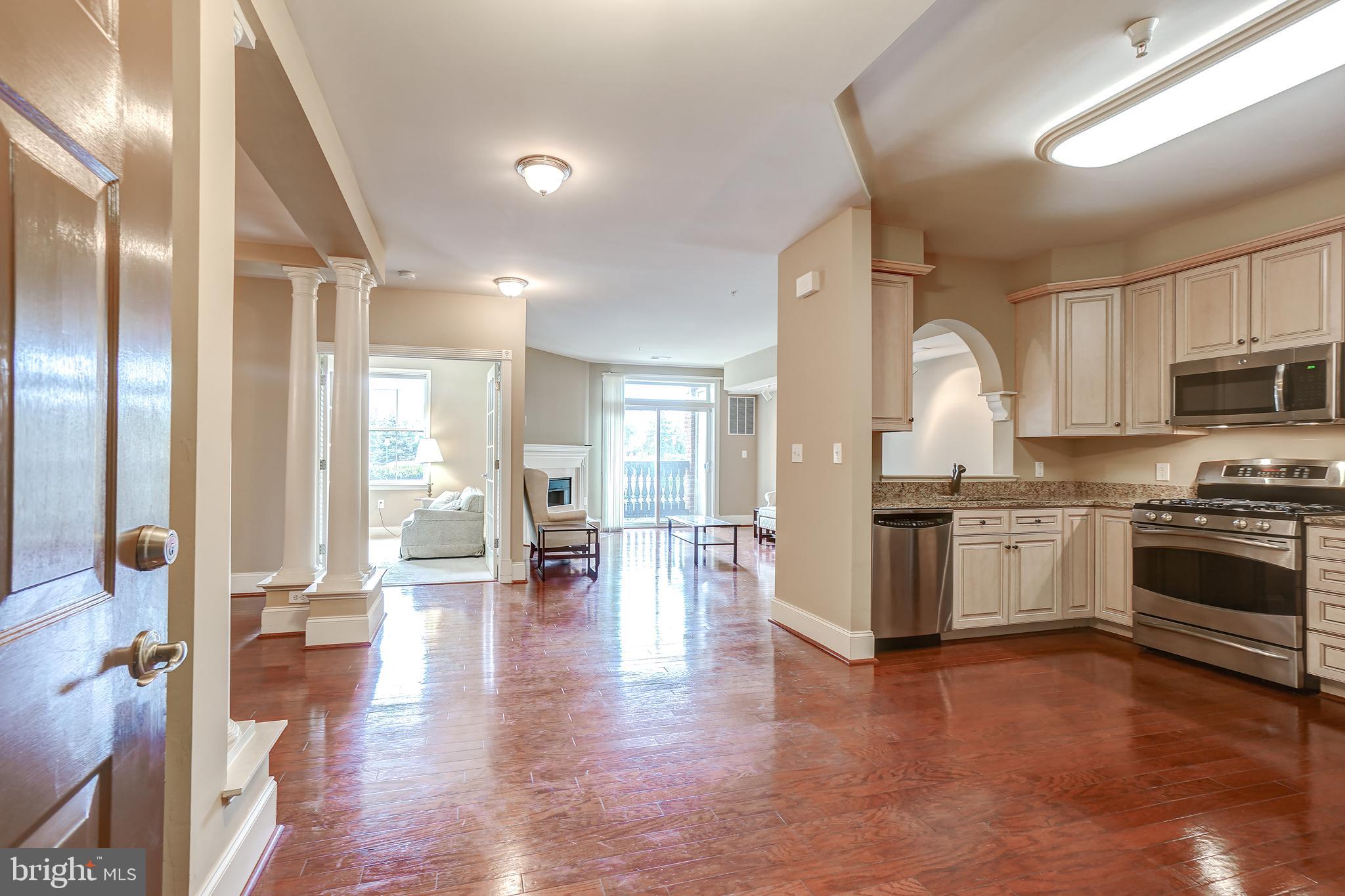 3030 Mill Island Parkway, Unit 109 Frederick, MD 21701 - Photo 3 of 20 a open kitchen with granite countertop a stove top oven a sink a dining table and chairs with wooden floor