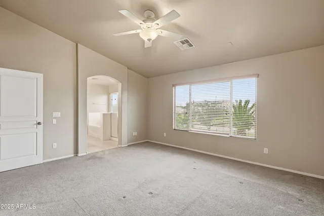 an empty room with chandelier fan and windows