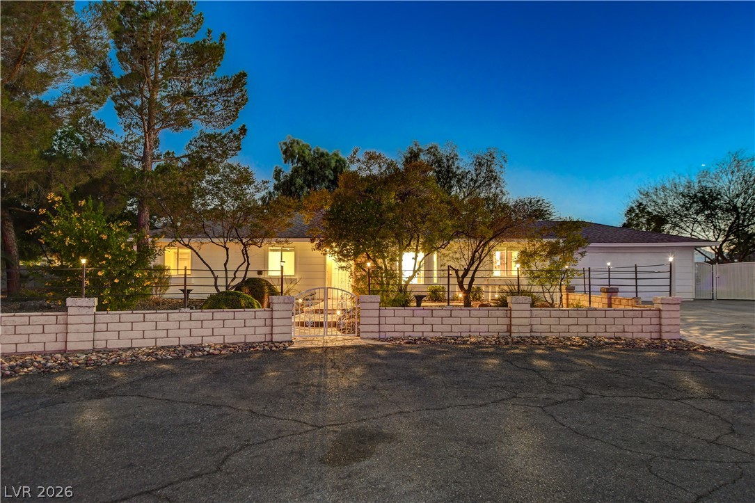 7631 Bermuda Road Las Vegas, NV 89123 - Photo 53 of 64 A welcoming home with a charming front yard, brick fencing, and a gated entrance illuminated at dusk.