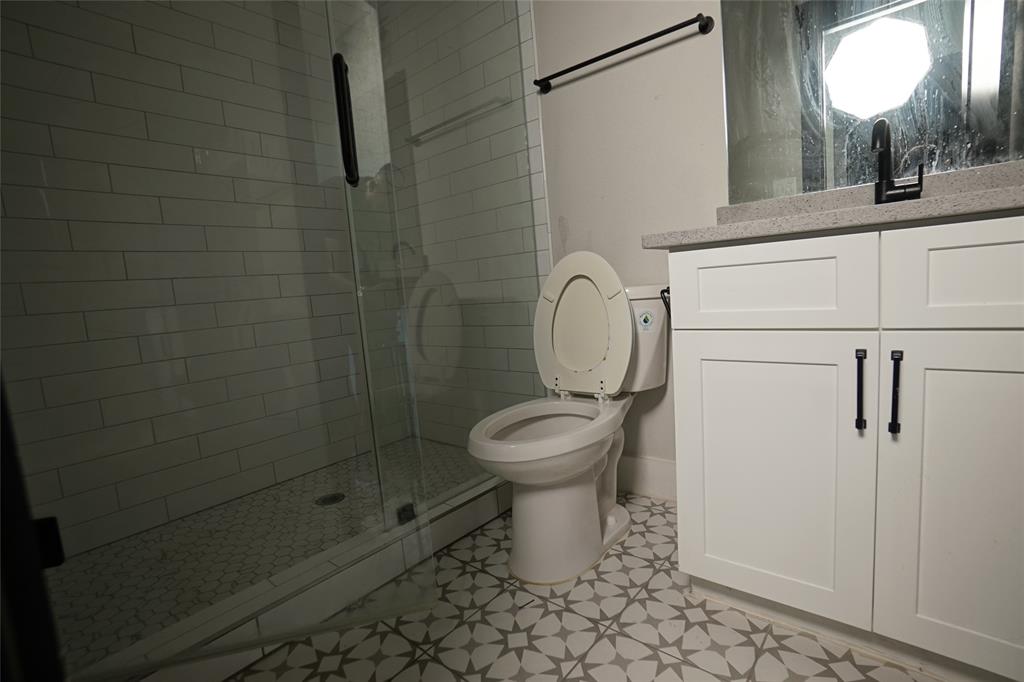 1764 Palladio Loop Princeton, TX 75407 - Photo 34 of 40 Bathroom featuring a glass-enclosed shower with subway tile surround, patterned floor tile, white vanity with stone countertop, and black fixtures