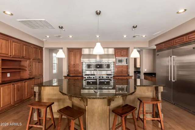 a kitchen with stainless steel appliances granite countertop a stove top oven a refrigerator a dining table and chairs with wooden floor