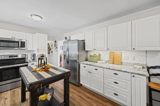 a open kitchen with stainless steel appliances granite countertop a stove top oven a sink dishwasher white cabinets and chairs with wooden floor