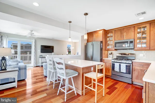 a view of kitchen with stainless steel appliances granite countertop a stove top oven a refrigerator a dining table and chairs with wooden floor