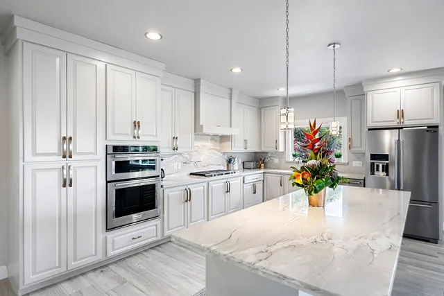a kitchen with stainless steel appliances kitchen island granite countertop a refrigerator a sink dishwasher and white cabinets with wooden floor