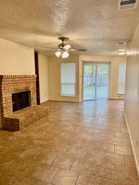9006 B Sedgemoor Trail Austin, TX 78748 - Photo 2 of 16 Unfurnished living room featuring a brick fireplace, a ceiling fan, a textured ceiling, and stone finish floors
